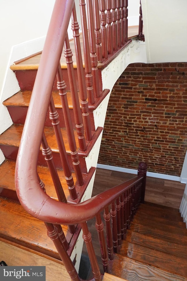 staircase with brick wall and wood-type flooring