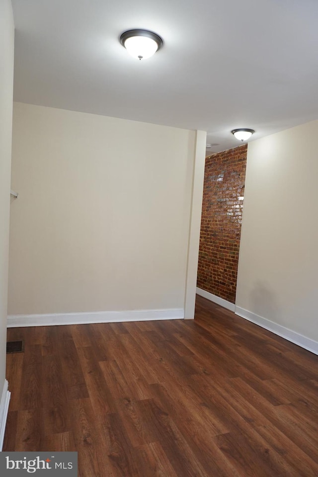 empty room with brick wall and dark hardwood / wood-style flooring