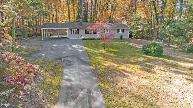 view of front facade featuring a chimney, a front yard, a view of trees, an attached carport, and driveway