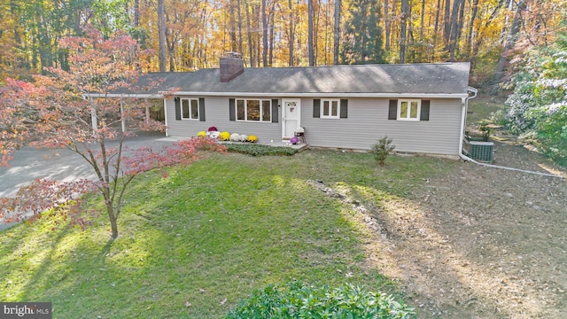 ranch-style house featuring a forest view, a chimney, a front lawn, and central AC unit