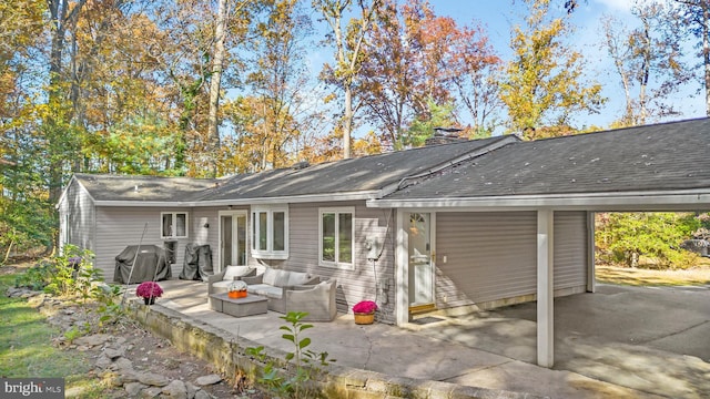 back of property with a shingled roof, a patio, a chimney, outdoor lounge area, and a carport