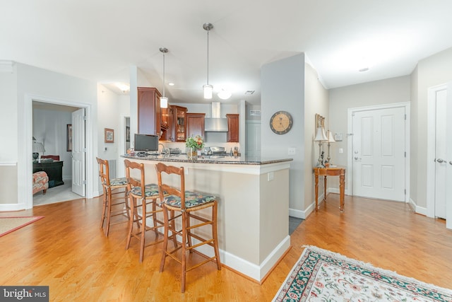 kitchen with pendant lighting, wall chimney range hood, kitchen peninsula, and light wood-type flooring