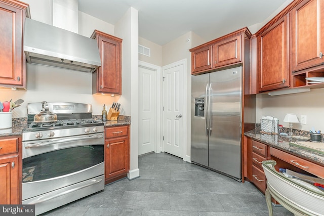 kitchen featuring tile patterned flooring, stainless steel appliances, dark stone counters, and wall chimney range hood