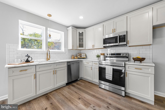 kitchen with light hardwood / wood-style flooring, hanging light fixtures, sink, white cabinets, and appliances with stainless steel finishes