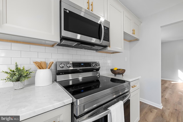 kitchen with light stone countertops, light wood-type flooring, white cabinetry, appliances with stainless steel finishes, and tasteful backsplash