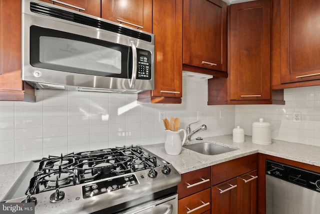 kitchen with light stone counters, stainless steel appliances, sink, and backsplash