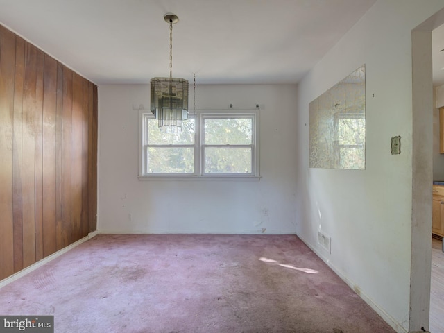 unfurnished dining area featuring wood walls, a chandelier, and carpet floors