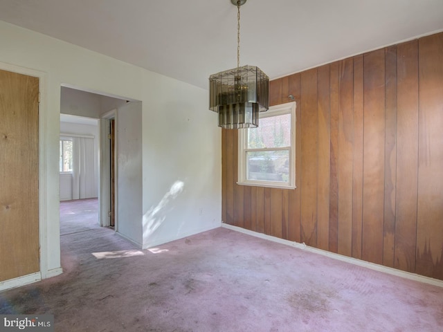 unfurnished dining area featuring an inviting chandelier, wooden walls, and carpet