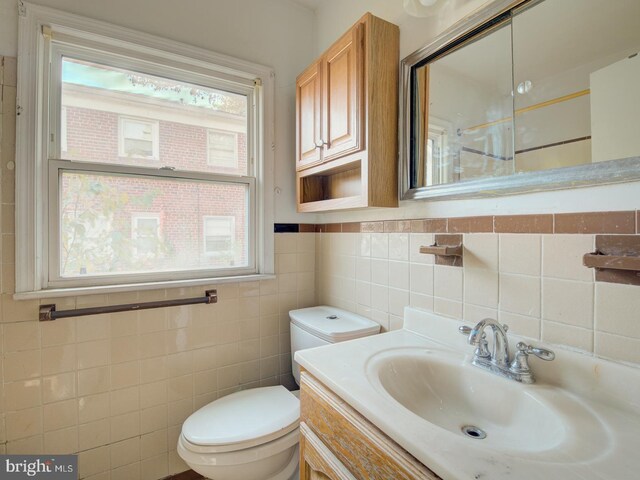 bathroom with toilet, vanity, tile walls, and a wealth of natural light