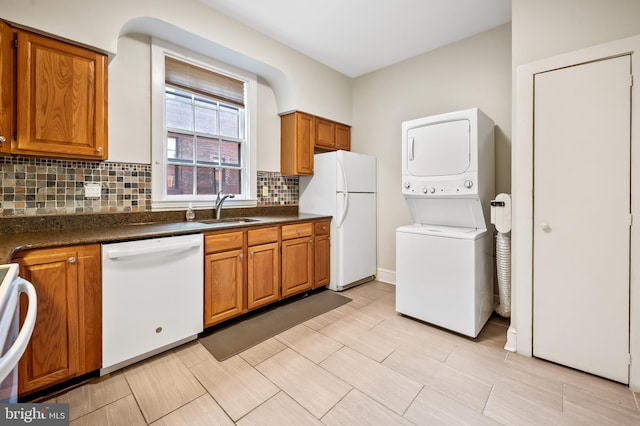 kitchen with white appliances, backsplash, sink, and stacked washer and clothes dryer