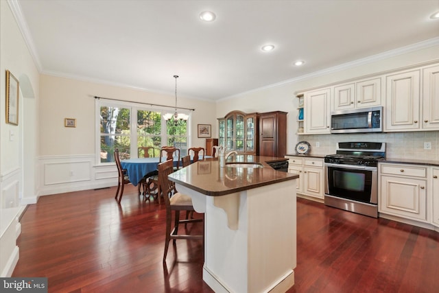 kitchen featuring dark wood-type flooring, an island with sink, a breakfast bar, pendant lighting, and appliances with stainless steel finishes