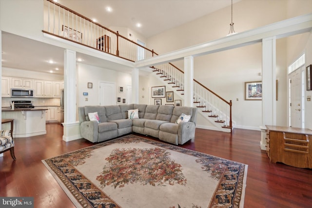 living room featuring a towering ceiling, dark hardwood / wood-style floors, and decorative columns