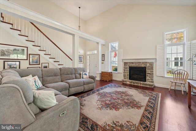 living room with dark wood-type flooring, a stone fireplace, high vaulted ceiling, and a healthy amount of sunlight