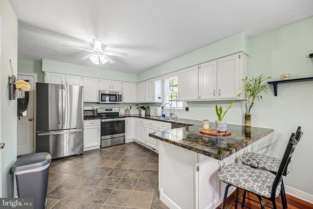 kitchen featuring kitchen peninsula, appliances with stainless steel finishes, a kitchen bar, dark stone countertops, and white cabinetry