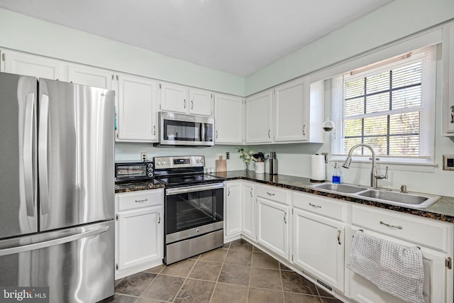 kitchen with stainless steel appliances, white cabinetry, dark stone countertops, and sink