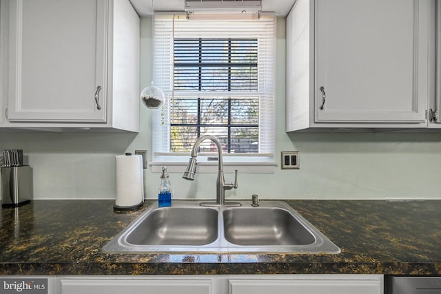 kitchen with a healthy amount of sunlight, white cabinetry, sink, and dark stone counters