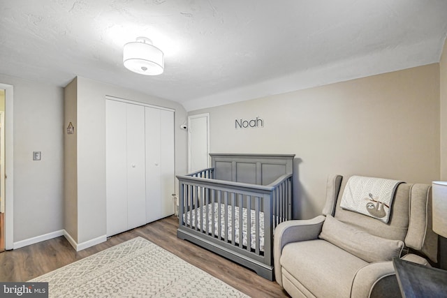 bedroom featuring a crib, dark wood-type flooring, and a closet