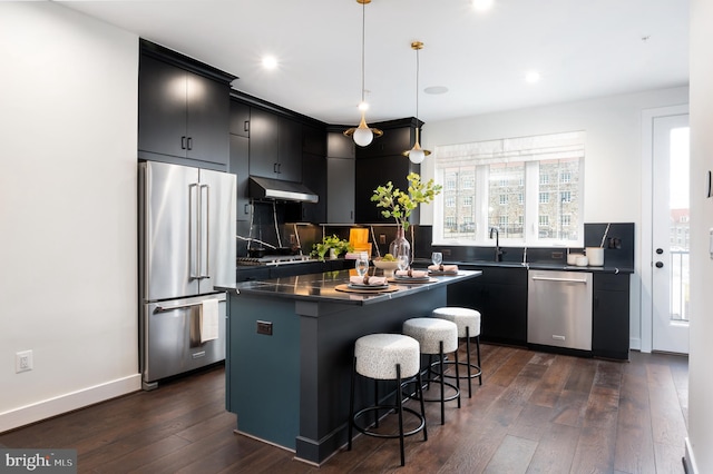 kitchen featuring appliances with stainless steel finishes, a kitchen island, pendant lighting, dark wood-type flooring, and a breakfast bar area