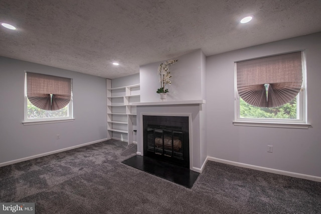 unfurnished living room featuring dark carpet, a textured ceiling, and a healthy amount of sunlight