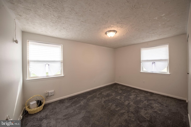 empty room with dark colored carpet, a textured ceiling, and plenty of natural light