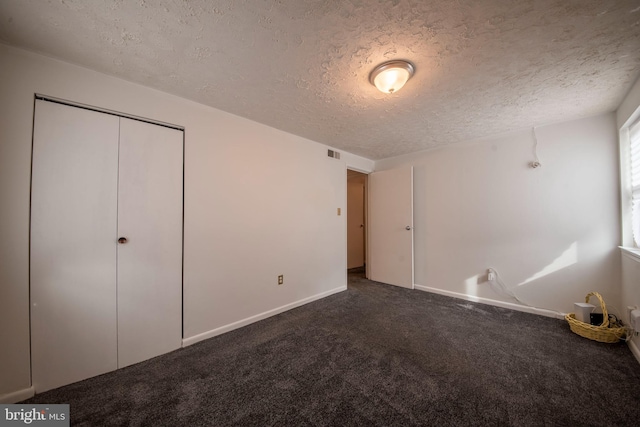 unfurnished bedroom featuring dark colored carpet, a textured ceiling, and a closet