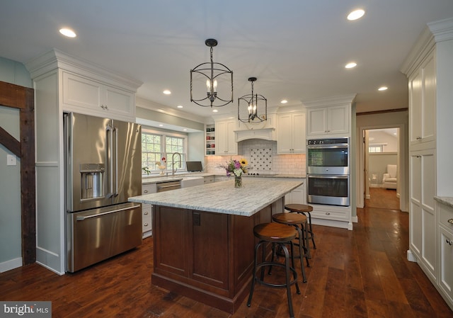 kitchen with a kitchen island, dark wood-type flooring, stainless steel appliances, light stone countertops, and pendant lighting