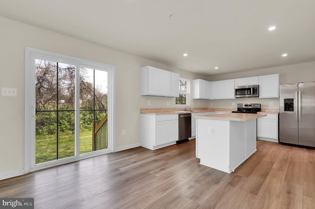 kitchen with a wealth of natural light, a kitchen island, appliances with stainless steel finishes, and light wood-type flooring