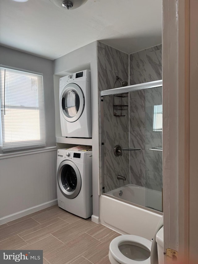 bathroom featuring enclosed tub / shower combo, stacked washer and clothes dryer, and toilet