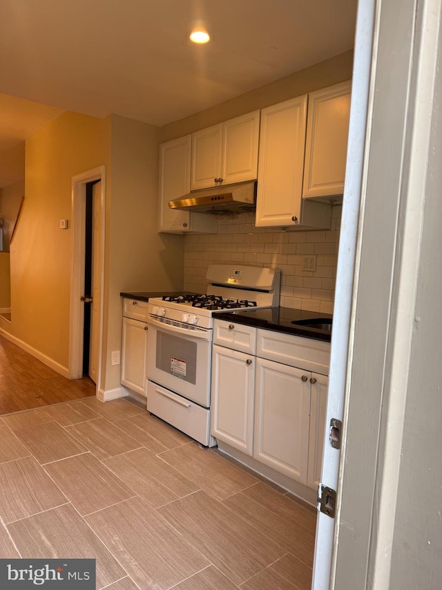 kitchen with white gas range, backsplash, light wood-type flooring, and white cabinets