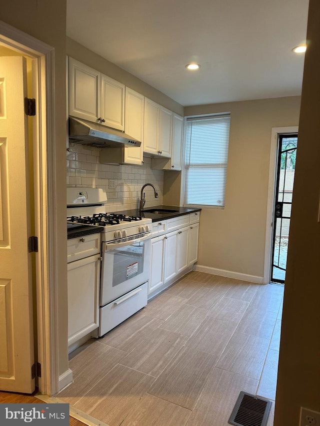 kitchen with white cabinets, backsplash, white gas stove, light hardwood / wood-style flooring, and sink