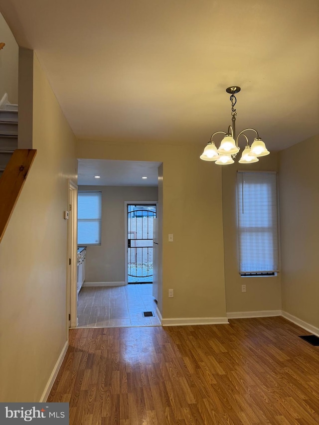 unfurnished dining area with an inviting chandelier and hardwood / wood-style flooring