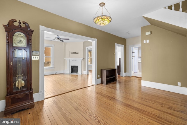 unfurnished living room featuring a ceiling fan, baseboards, a fireplace, and light wood finished floors