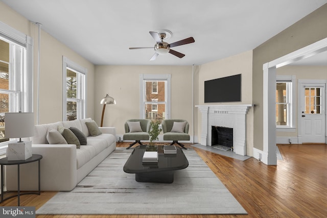 living room with a ceiling fan, a brick fireplace, baseboards, and light wood finished floors