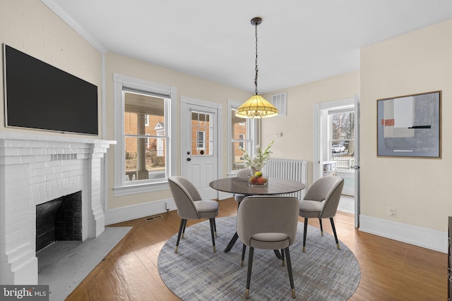 dining space with a fireplace, wood finished floors, visible vents, and baseboards