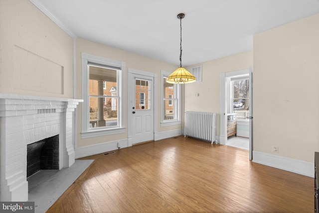 unfurnished dining area featuring a healthy amount of sunlight, light wood-style floors, radiator heating unit, and a brick fireplace