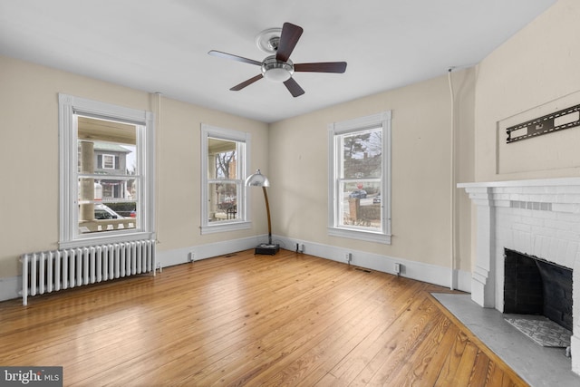 unfurnished living room with a brick fireplace, radiator heating unit, plenty of natural light, and wood finished floors