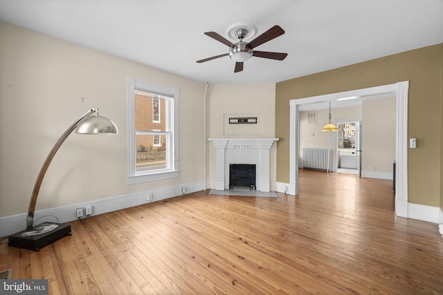 unfurnished living room featuring ceiling fan, wood finished floors, baseboards, a brick fireplace, and radiator