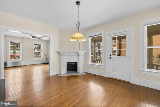 unfurnished living room featuring a fireplace, radiator, visible vents, wood finished floors, and baseboards