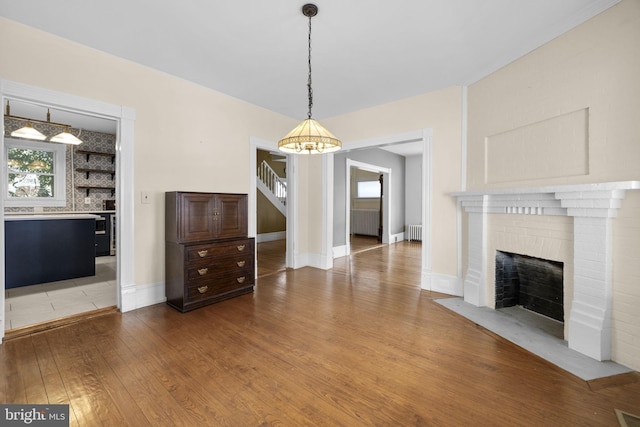 unfurnished living room with baseboards, light wood finished floors, a fireplace, and radiator