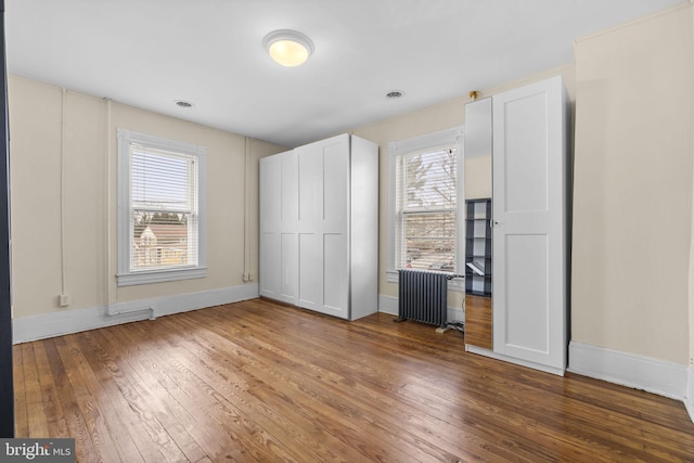 unfurnished bedroom with baseboards, dark wood finished floors, visible vents, and radiator heating unit