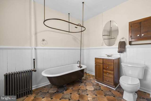 full bathroom with a freestanding tub, toilet, a wainscoted wall, vanity, and radiator heating unit