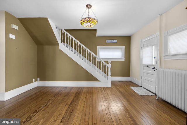 entrance foyer with baseboards, radiator heating unit, stairway, and wood finished floors