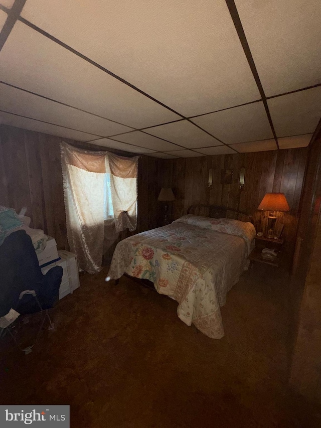 carpeted bedroom with a paneled ceiling and wooden walls