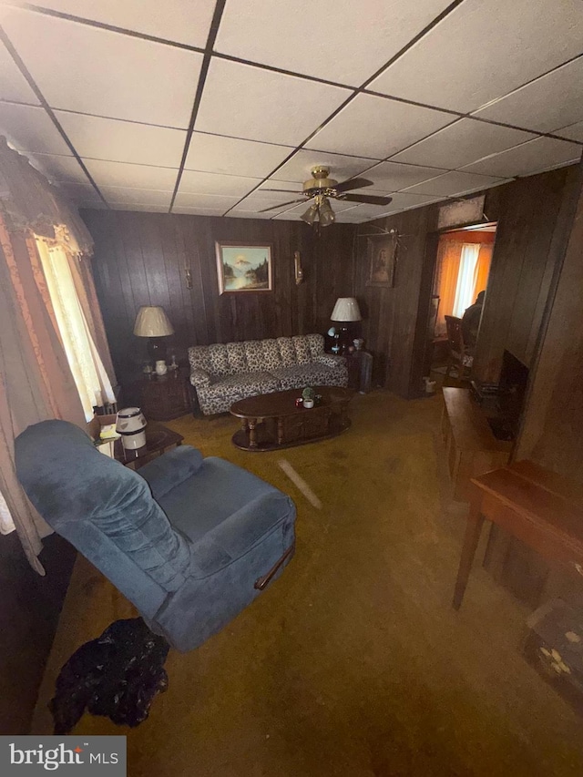 carpeted living room with wood walls, a paneled ceiling, and ceiling fan