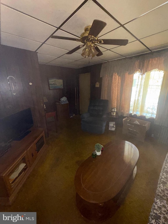 living room featuring wood walls, a paneled ceiling, carpet flooring, and ceiling fan