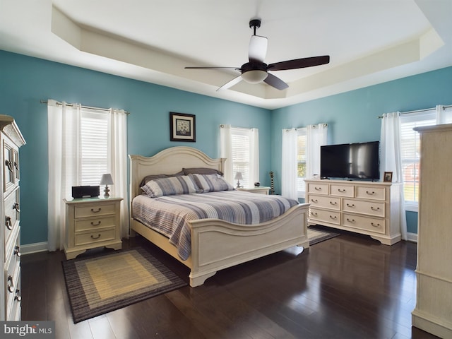 bedroom featuring ceiling fan, a tray ceiling, and dark hardwood / wood-style flooring