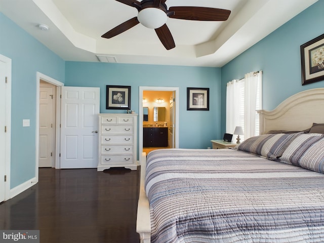 bedroom featuring ensuite bath, ceiling fan, a tray ceiling, and dark hardwood / wood-style flooring