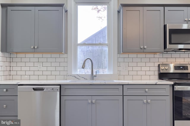 kitchen featuring decorative backsplash, appliances with stainless steel finishes, light stone countertops, gray cabinets, and sink