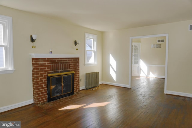 unfurnished living room with radiator, dark hardwood / wood-style flooring, and a brick fireplace