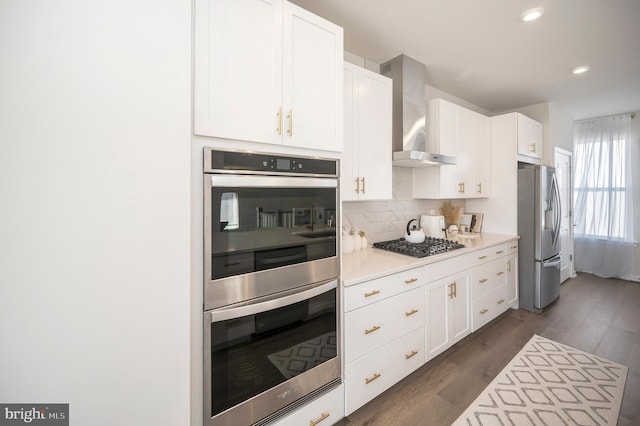 kitchen with wall chimney range hood, appliances with stainless steel finishes, dark hardwood / wood-style floors, and white cabinets